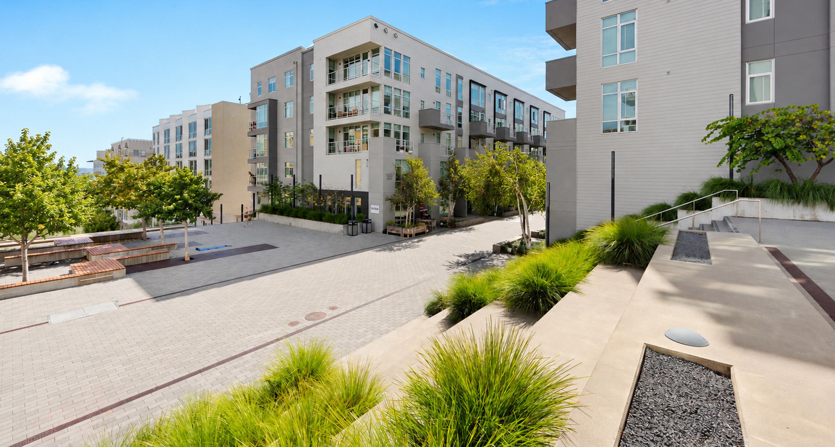 Alchemy contemporary apartment building in Hayes Valley with clean lines, large windows, and private balconies, framed by sleek siding and light neutral tones. Trees line the paved courtyard below, giving the space a modern, walkable neighborhood feel.