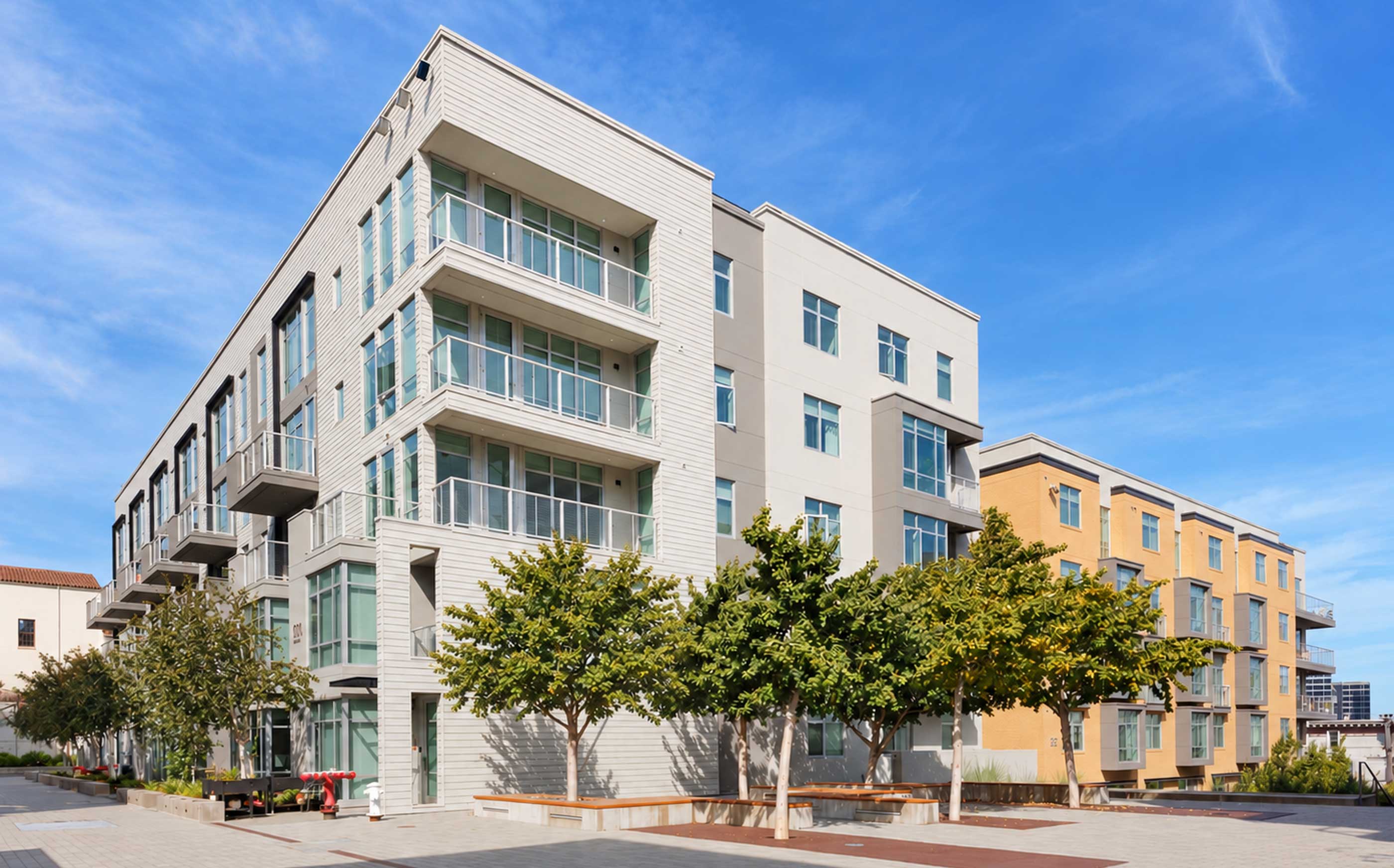 Alchemy contemporary apartment building in Hayes Valley with clean lines, large windows, and private balconies, framed by sleek siding and light neutral tones. Young trees line the paved courtyard below, giving the space a modern, walkable neighborhood feel.