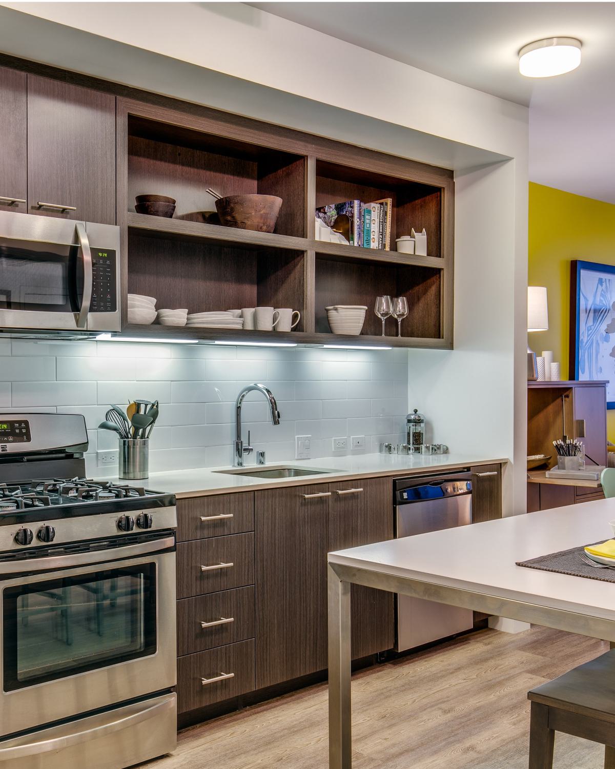 Contemporary kitchen with stainless steel appliances, wood cabinetry, open shelving, under-cabinet lighting, and a sleek island with a built-in dining area.