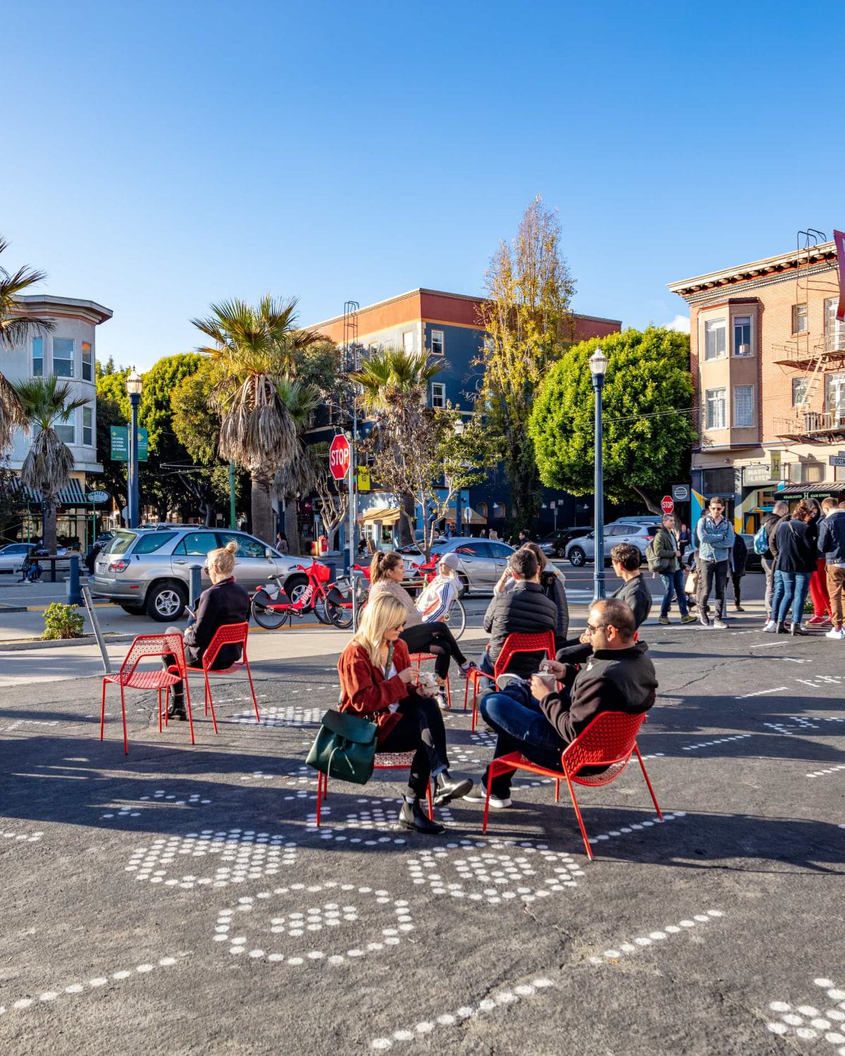 People relaxing on red chairs at Patricia’s Green in Hayes Valley, a popular public gathering space with street art, palm trees, and vibrant urban surroundings.