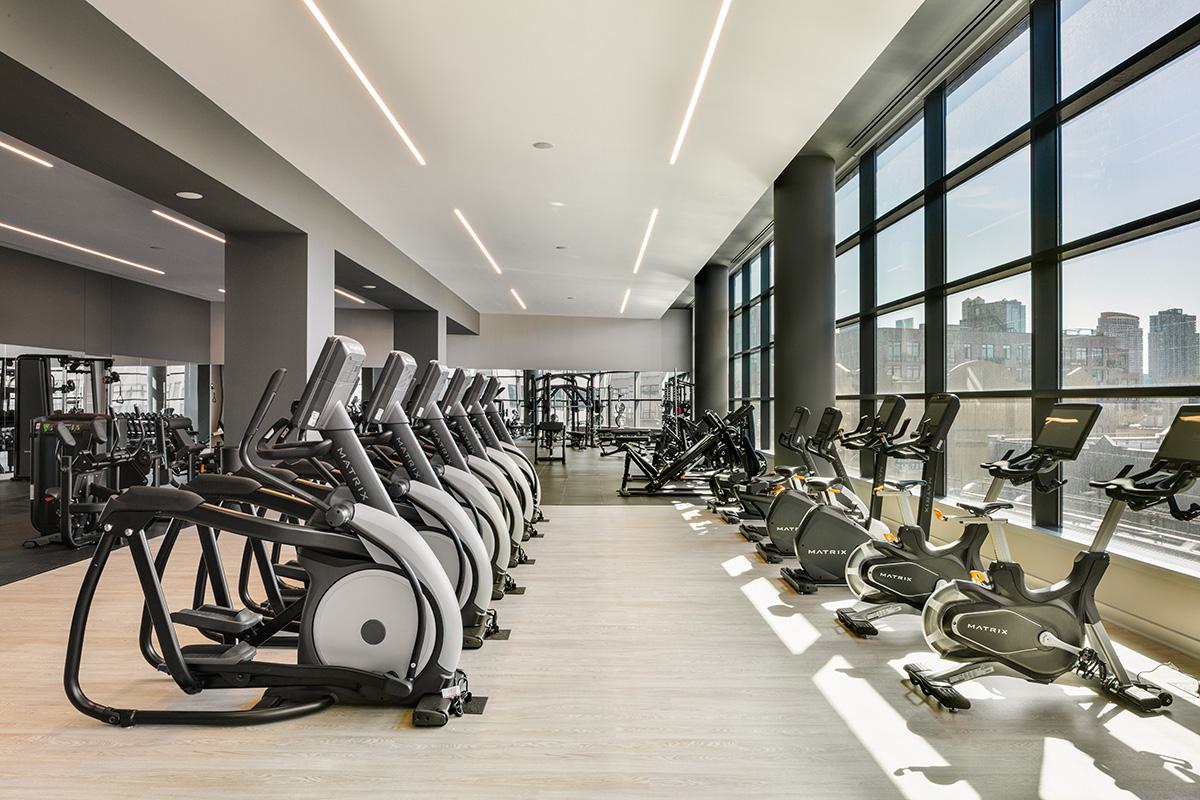 Spacious fitness center with rows of cardio machines and large windows overlooking the manhattan skyline