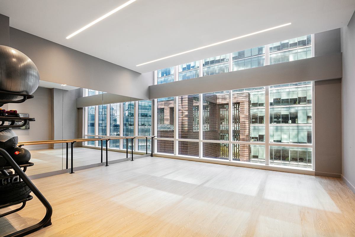 Bright yoga and pilates studio with mirrored walls, ballet barre, and city views through tall windows.