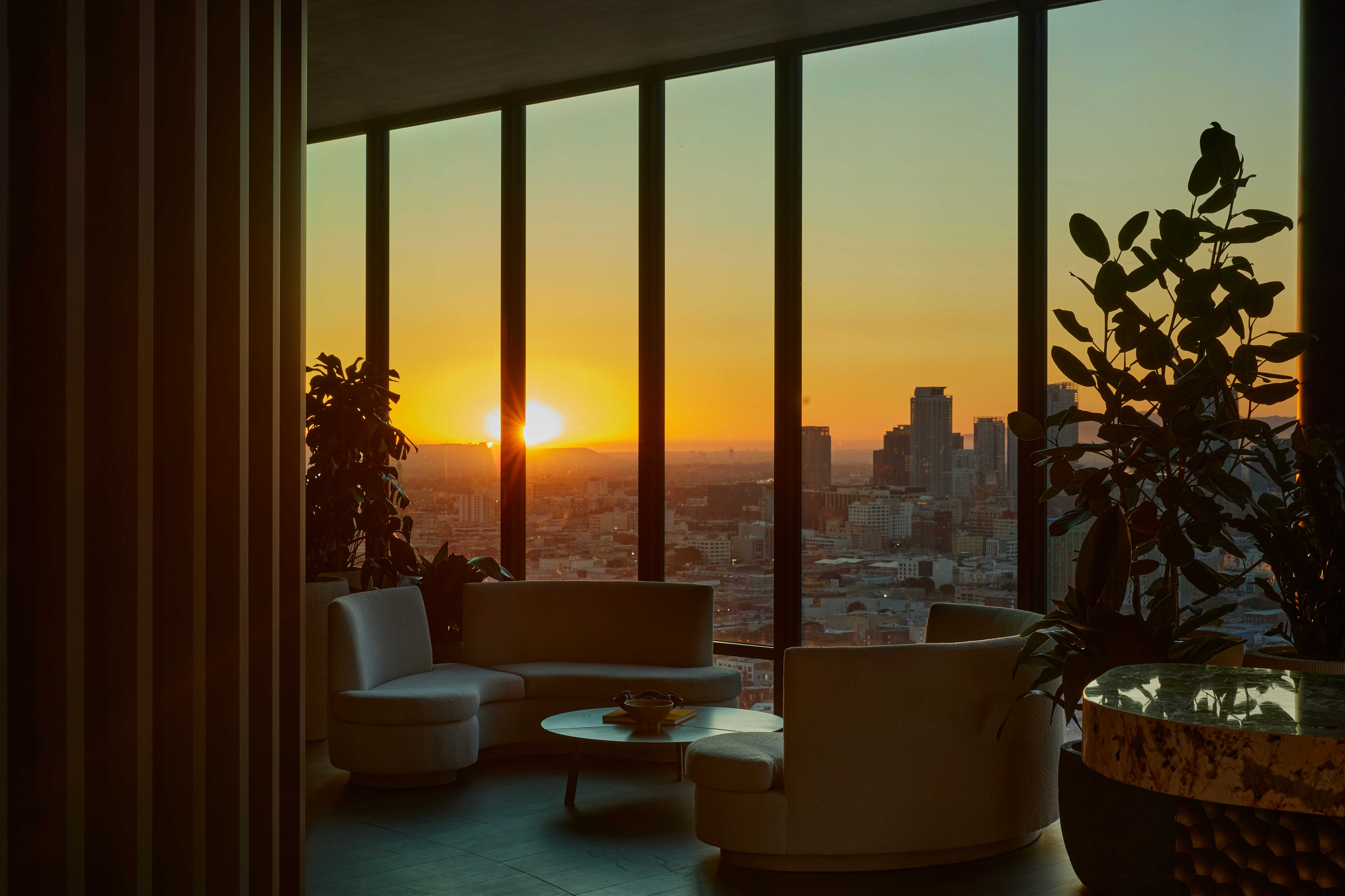 Rooftop lounge at Alloy Apartments with modern seating and plants, showcasing a dramatic sunset and panoramic views of downtown Los Angeles.