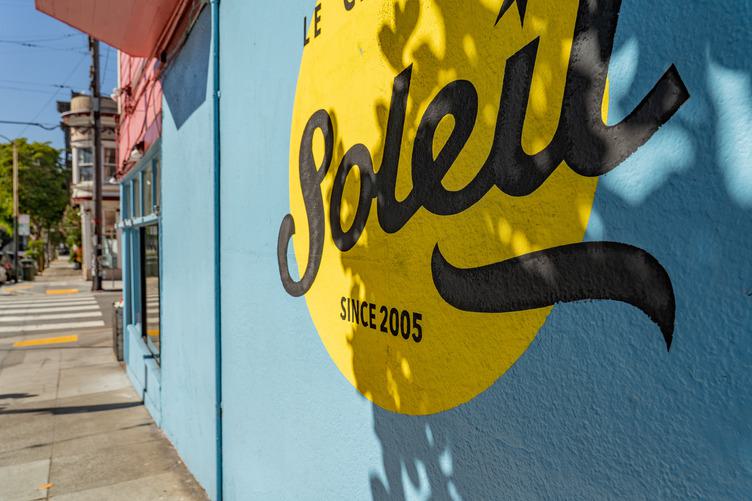 Mural-style storefront wall in San Francisco’s Lower Haight, featuring bold painted lettering and a bright yellow circle along a sunlit sidewalk.