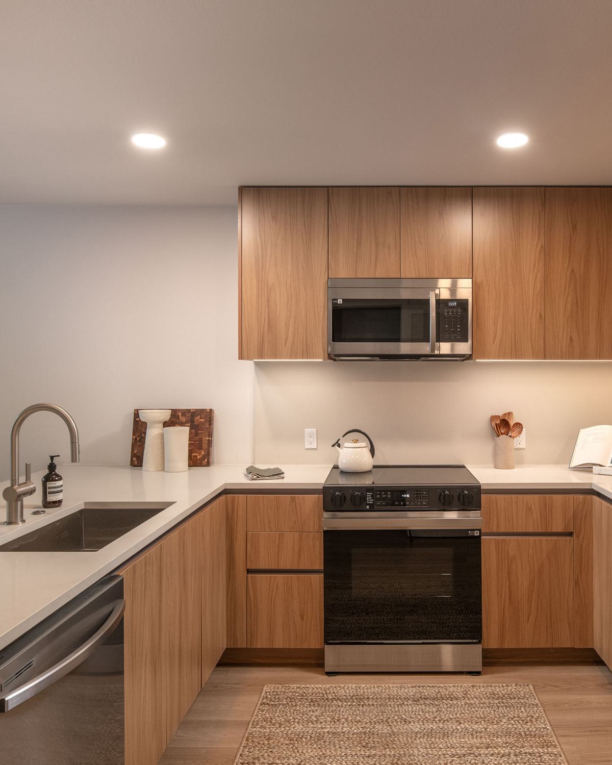 Contemporary kitchen with light wood cabinetry, sleek island seating, luxe appliances,  and floor to ceiling windows offering sunny Hillcrest views and abundant natural light.