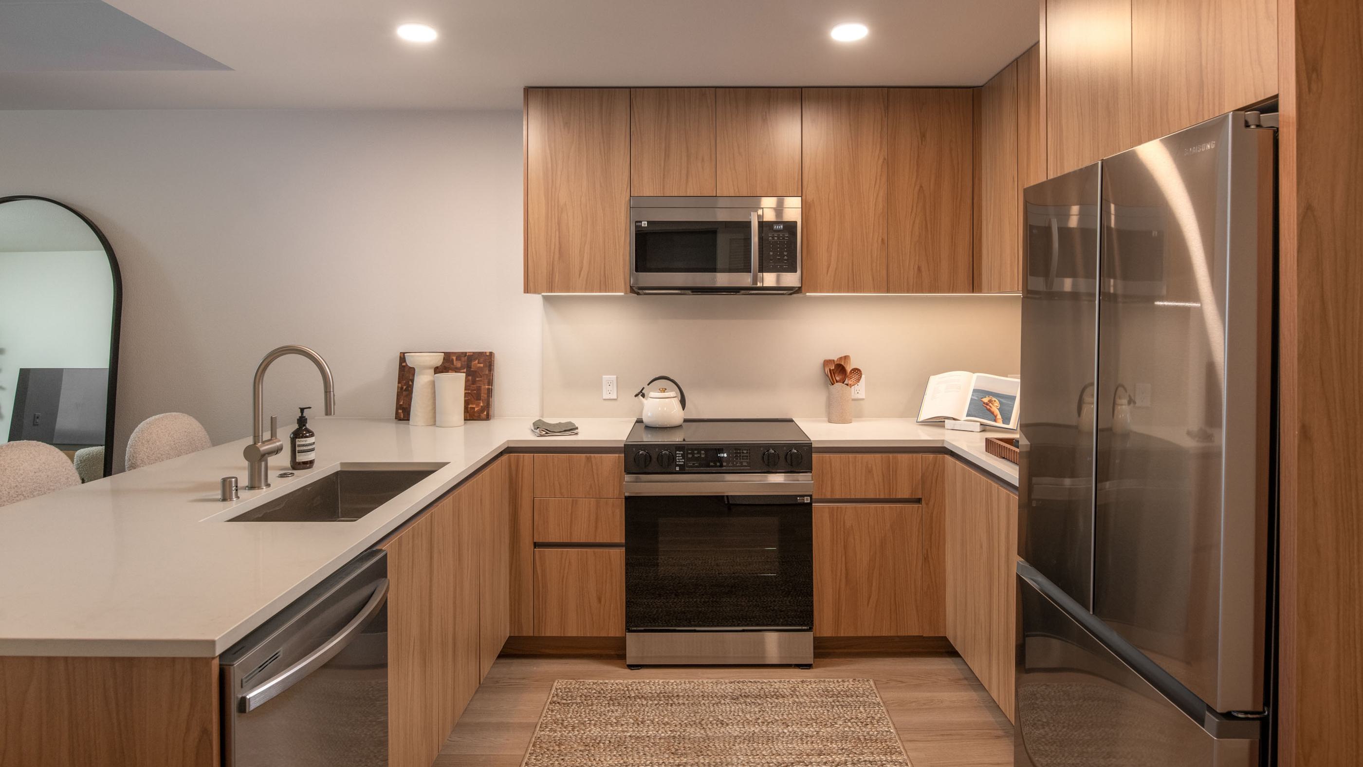 Contemporary kitchen with light wood cabinetry, sleek island seating, luxe appliances,  and floor to ceiling windows offering sunny Hillcrest views and abundant natural light.