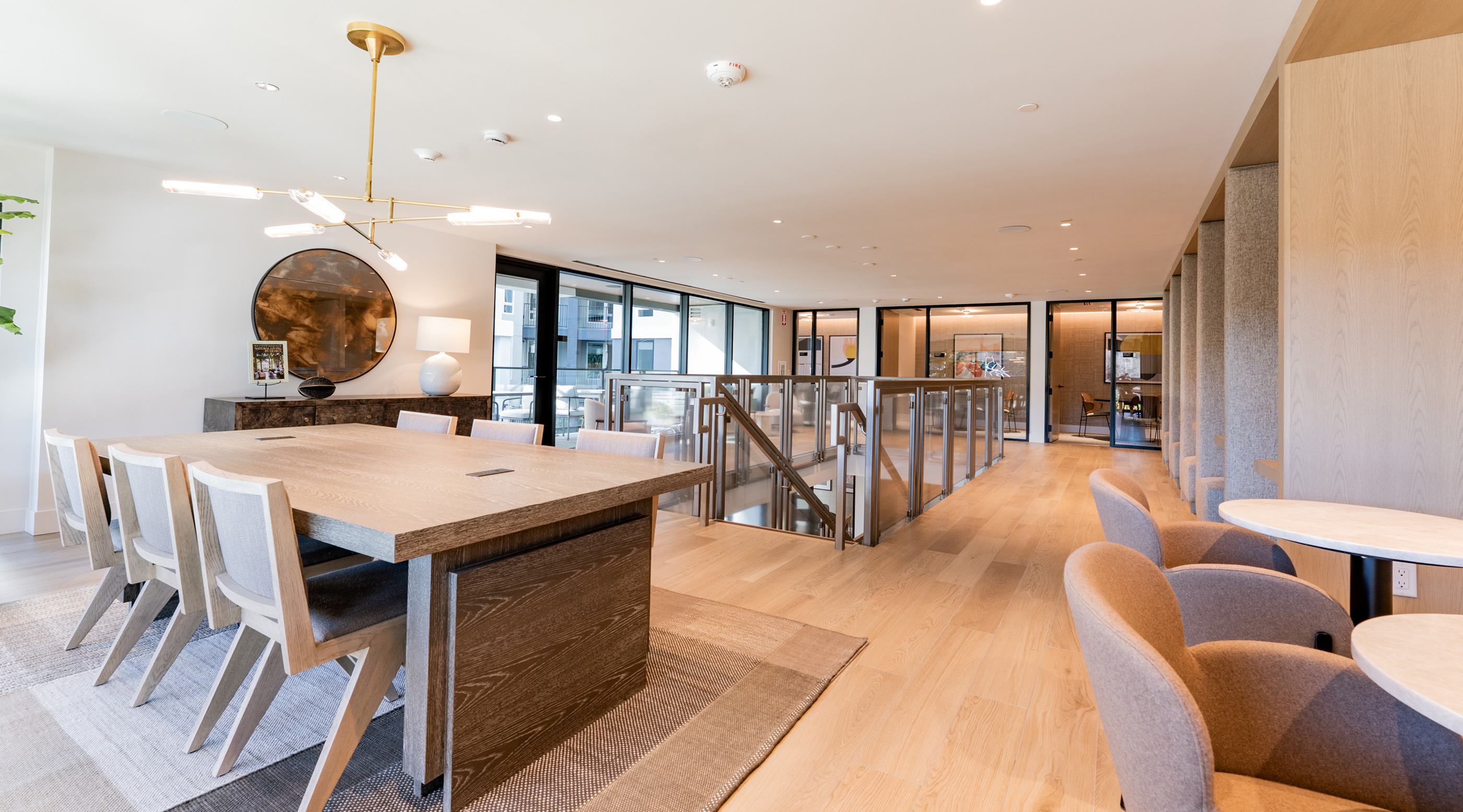 Modern,  mid-rise Revery apartment building at dusk, with sleek glass corner windows, warm interior lighting, and the name “REVERY” illuminated at the top. The design features clean lines, wood and brick textures, and landscaped trees lining the sidewalk for an inviting urban presence.