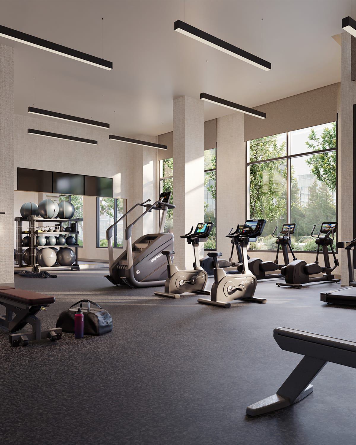 A spacious, light-filled fitness center equipped with treadmills, bikes, free weights, and resistance machines. Floor-to-ceiling windows overlook landscaped greenery, creating a calm and energizing workout environment.