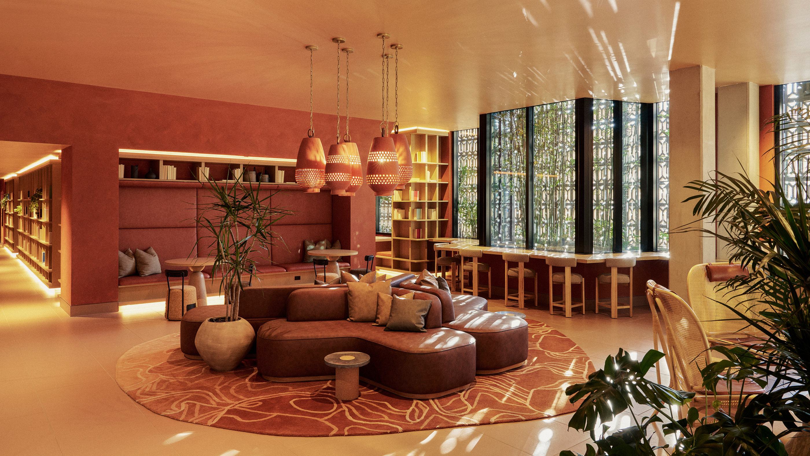A richly textured lobby at Rowyn Apartments featuring warm terracotta tones, sculptural pendant lighting, plush seating, curated bookshelves, and statement geometric wall panels—blending boutique hotel ambiance with elevated residential design.
