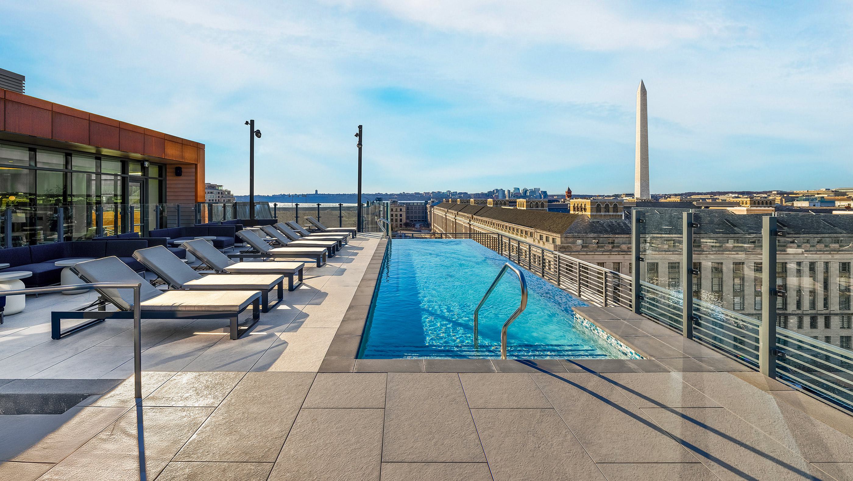 Rooftop lap pool at Annex on 12th with sun loungers and glass railing, overlooking downtown DC and the Washington Monument.