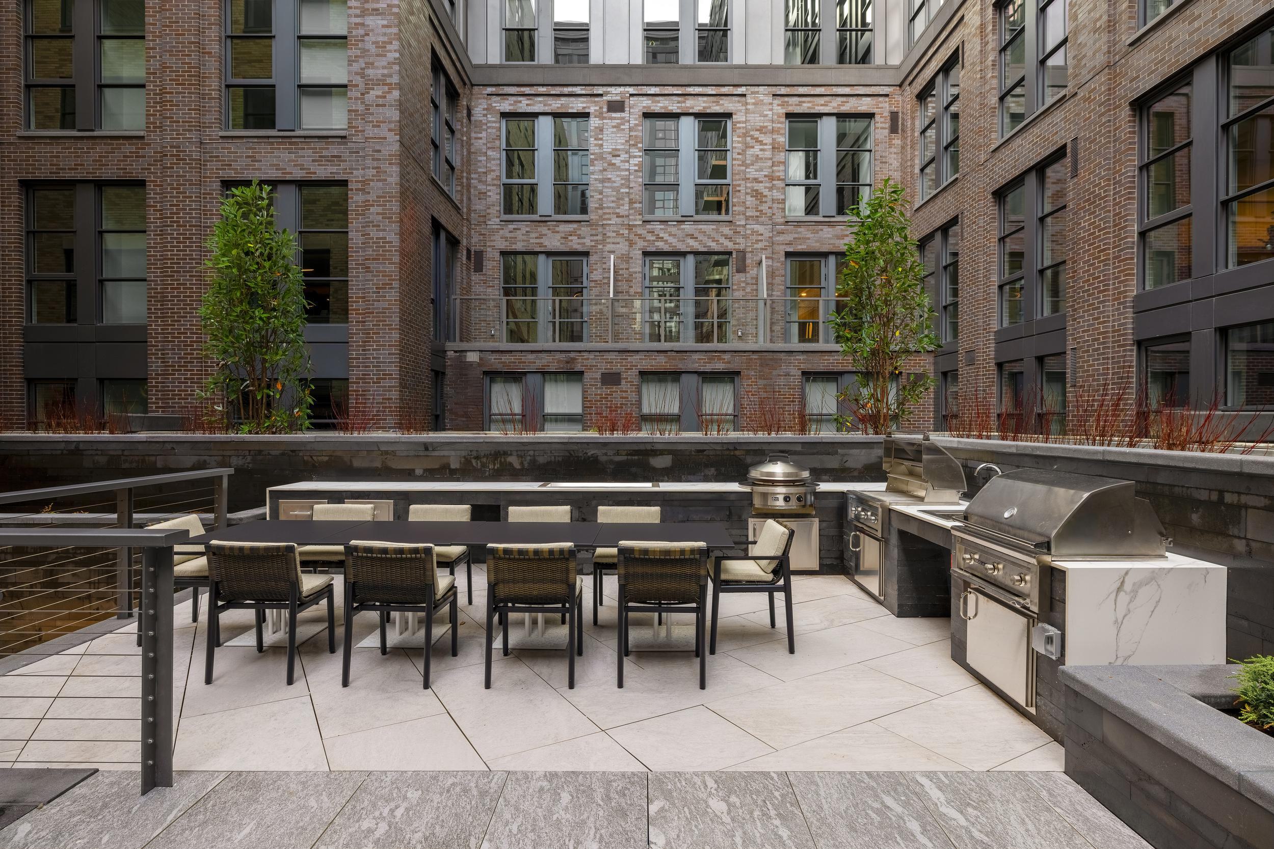 Outdoor grilling stations and long dining table in the courtyard at Annex on 12th, framed by planters and historic brick architecture.