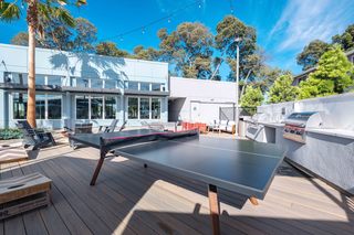 Modern outdoor courtyard at Admiral’s Cove featuring a sleek ping pong table, string lights, Adirondack chairs, and built-in stainless steel grilling stations.