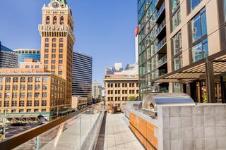 Scenic outdoor terrace at Atlas Apartments in Downtown Oakland featuring stainless steel BBQ grills and a wood-fired pizza oven with views of the Tribune Tower and city skyline.