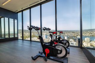 Close-up view of two stationary bikes positioned near expansive floor-to-ceiling windows overlooking Downtown Oakland and Lake Merritt from a high-rise fitness space.