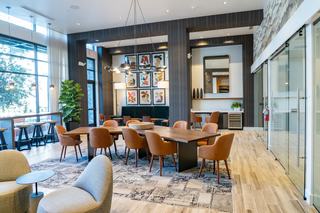 Sophisticated coworking space with a large wooden table, leather chairs, lounge seating, and floor-to-ceiling windows, featuring adjacent private meeting rooms with glass doors.
