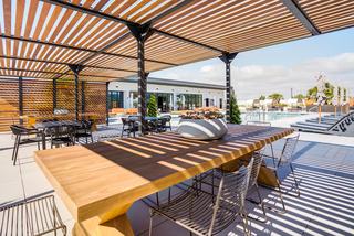 Rooftop terrace at The Asher with shaded pergola, wooden dining tables, modern chairs, and views of the pool deck with cabanas and lounge seating