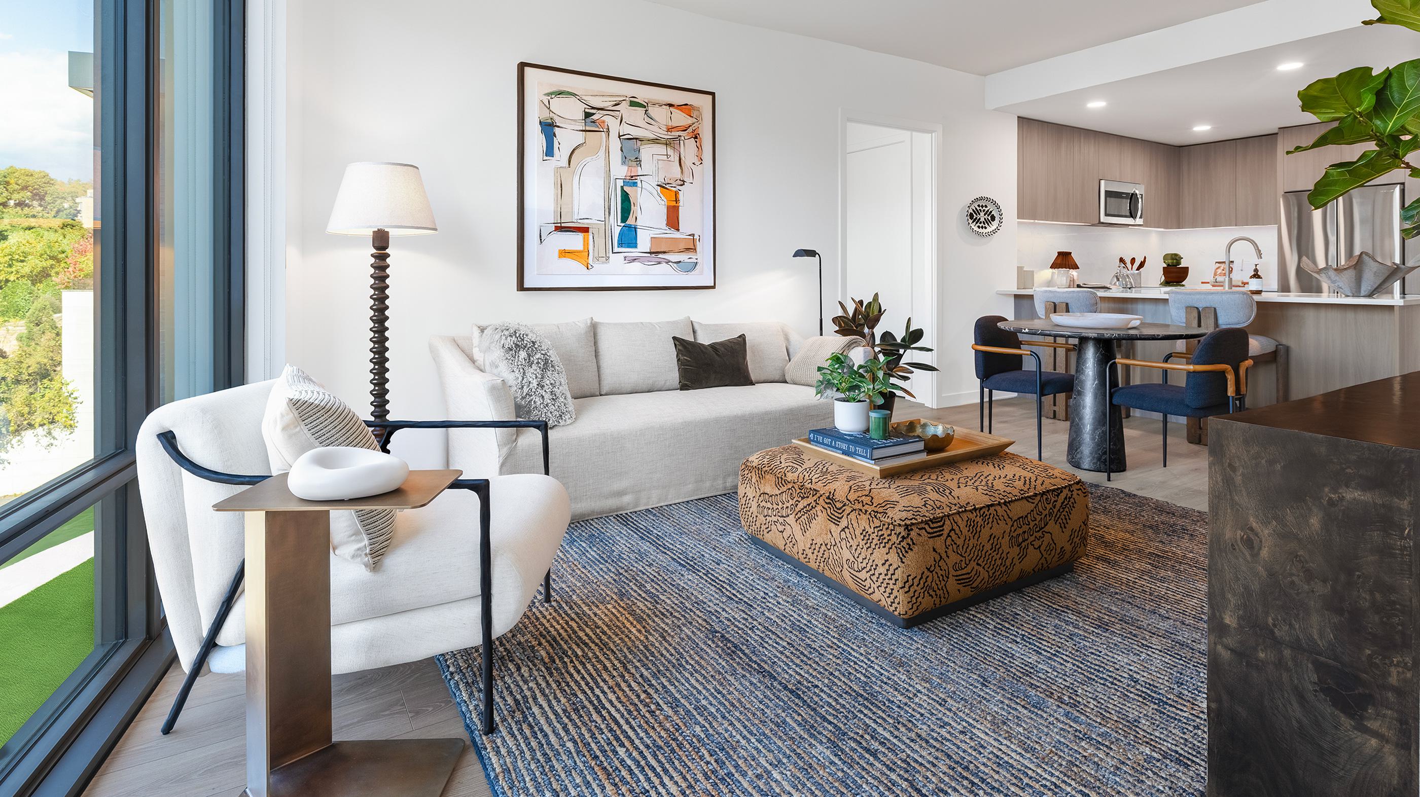 Spacious living area at Zephyr in Woodley Park, DC, featuring floor-to-ceiling windows, a neutral sectional sofa, modern lighting, and expansive views of the surrounding neighborhood and greenery.