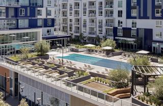 Aerial view of the South Pool at Vox, surrounded by lounge chairs, umbrellas, raised planters, and greenery, with an upper terrace featuring sectional seating areas and landscaped planters overlooking the pool deck.