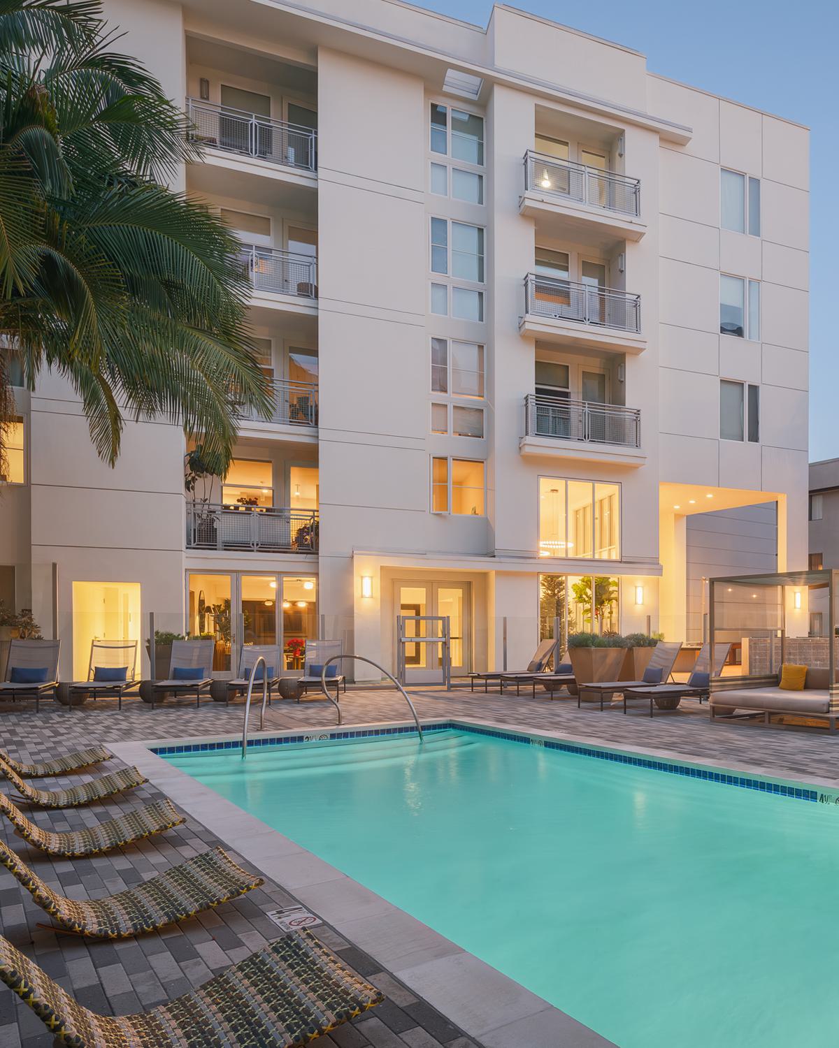 Sophisticated resident apartment building lounge with modern furniture, warm wood tones, and pendant lighting.