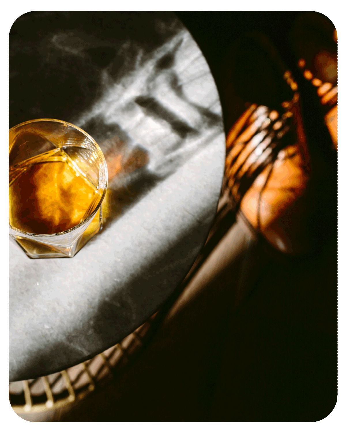 Glass of amber whiskey on a sunlit marble table.