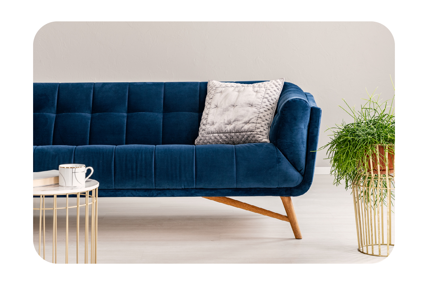 Modern living room scene with a blue velvet sofa, soft pillow, gold accent table, and potted plant.