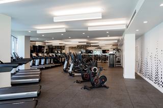 Spacious fitness center with rows of Life Fitness treadmills, Echelon stationary bikes, elliptical machines, and strength training equipment, featuring rubberized flooring, mirrored walls, and bright overhead lighting