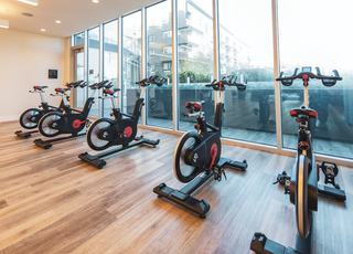 Bright spin studio with floor-to-ceiling windows, wood flooring, and rows of black-and-red Echelon stationary bikes arranged facing outward toward terrace views.