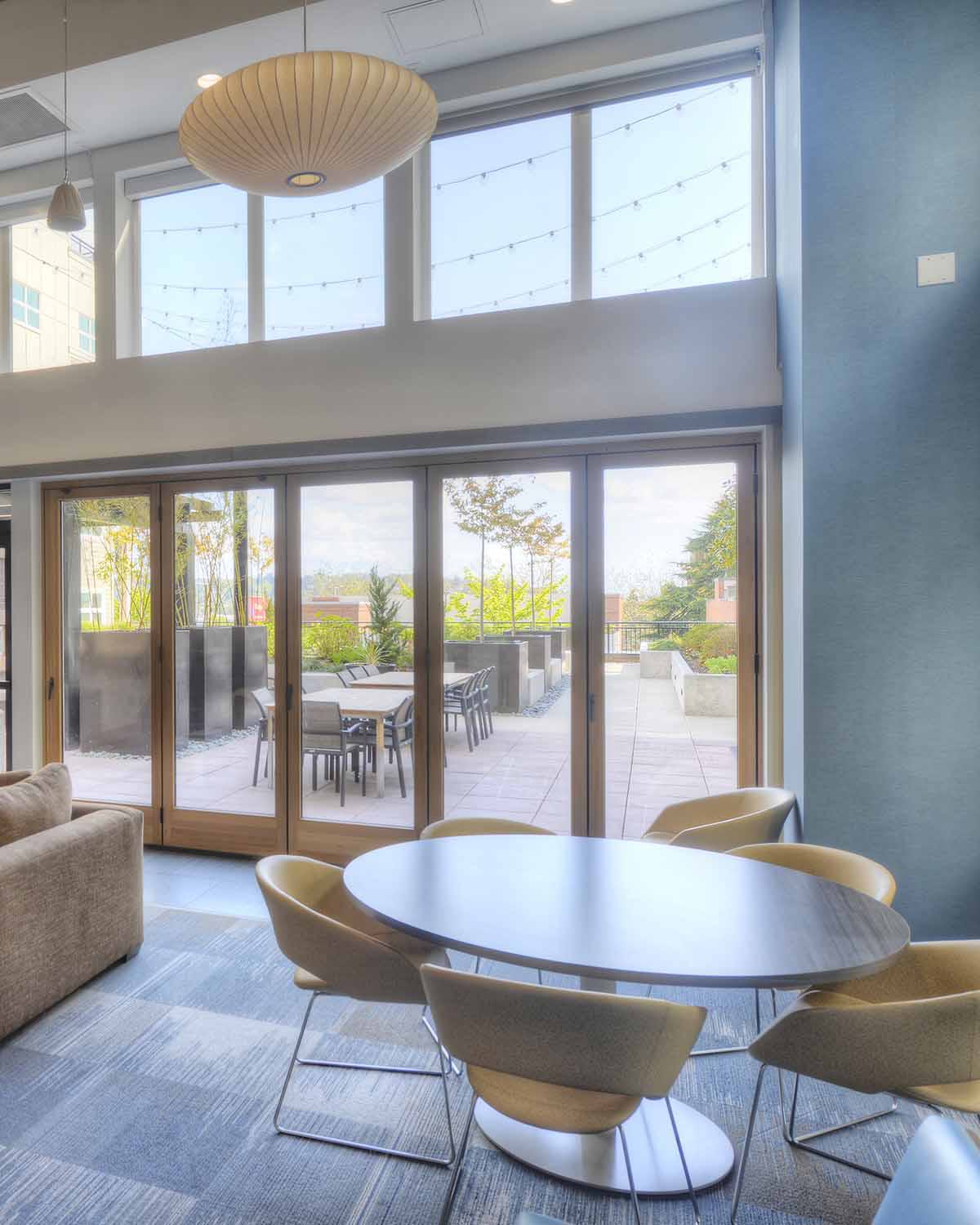 Modern resident lounge with cozy seating, a TV, and large windows opening to a furnished outdoor terrace.