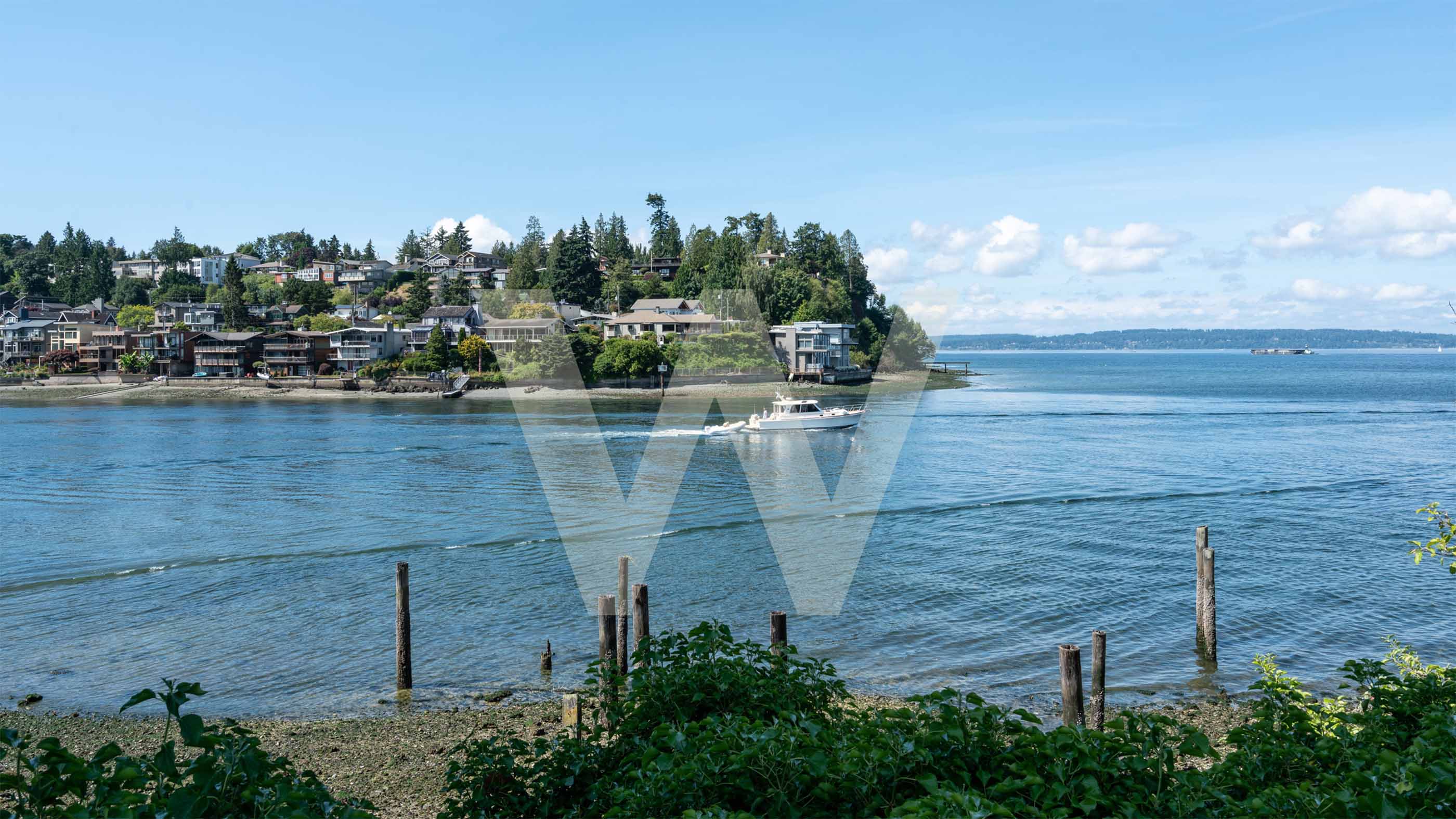 A small boat travels through Shilshole Bay with waterfront homes and greenery along Ballard’s scenic shoreline in Seattle, WA.