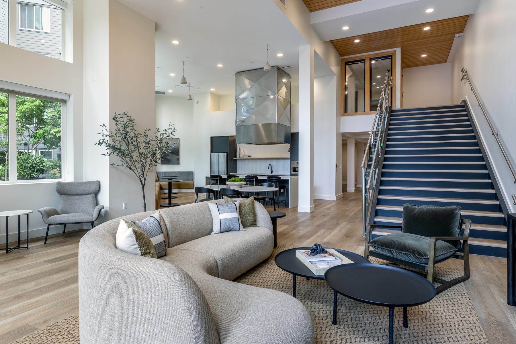 Modern resident lounge with a high ceiling, cozy seating, a wall-mounted TV, and access to an outdoor patio.