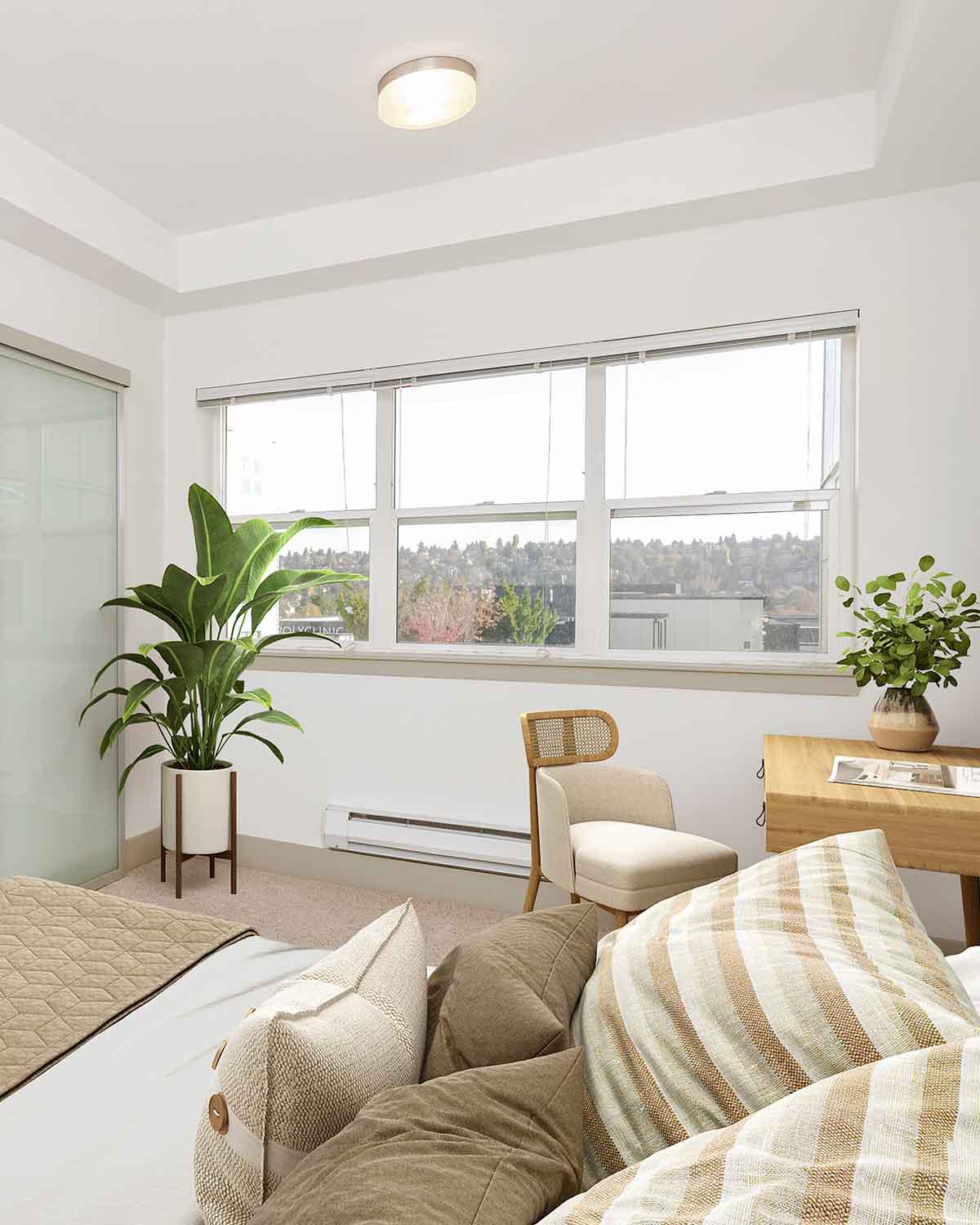 Bright bedroom in a Ballard, WA apartment featuring large windows with a view, neutral decor, cozy bedding, a desk, and green plants.