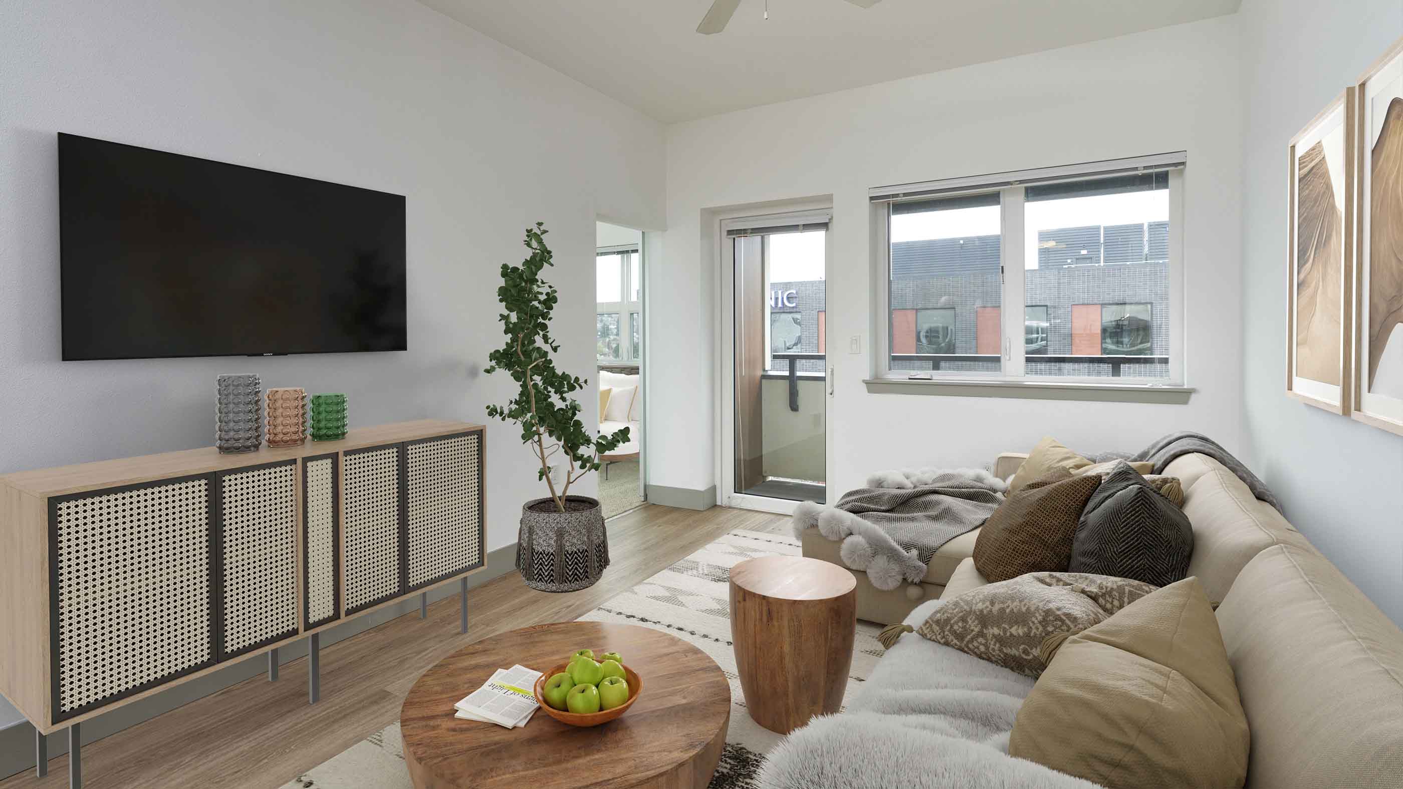 Cozy modern living room with a sectional sofa, wood accents, a mounted TV, and access to a private balcony with views of surrounding neighborhood in Ballard, Seattle.