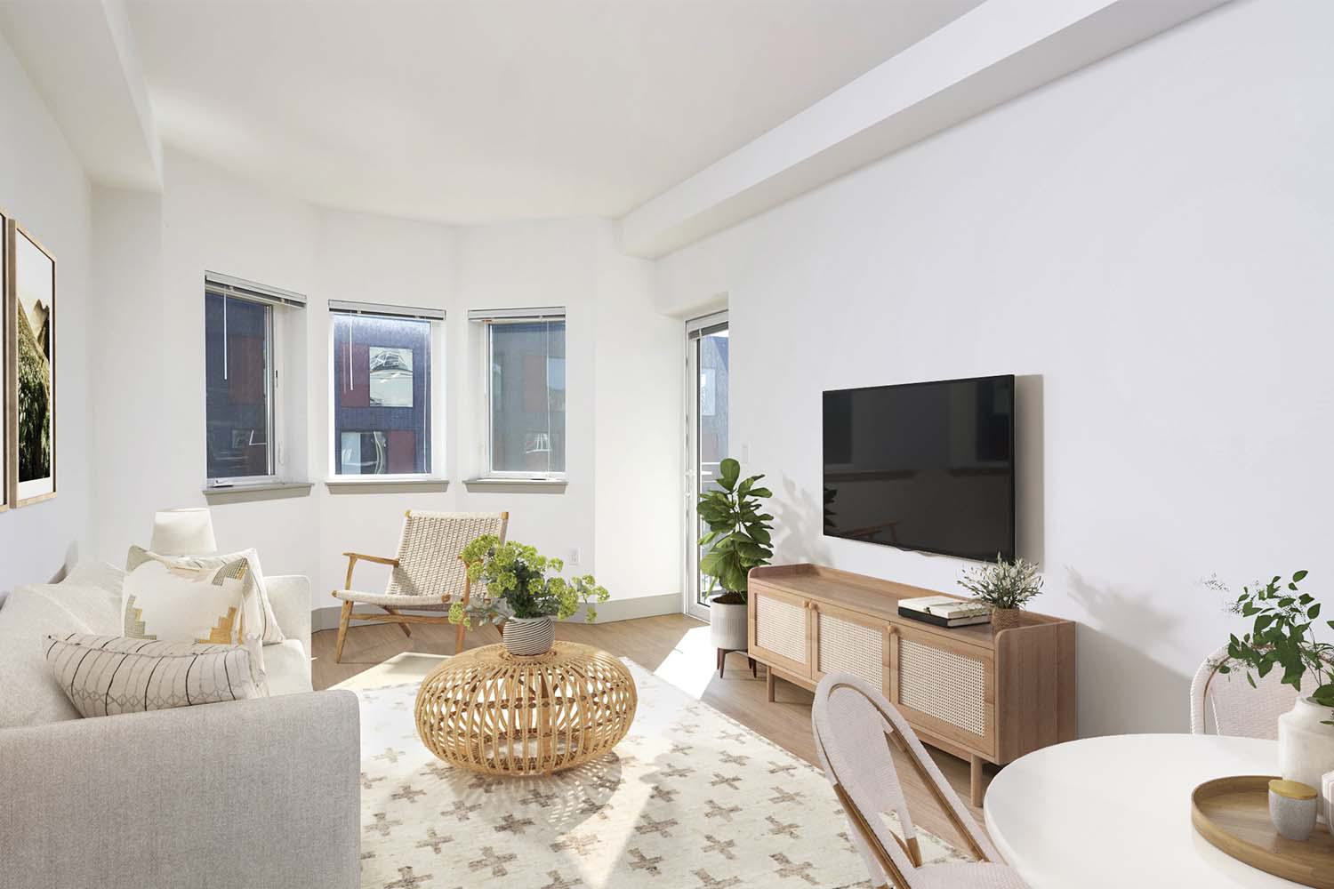 Bright, airy apartment living room with a bay window, neutral-toned furniture, woven accents, and access to a private balcony.