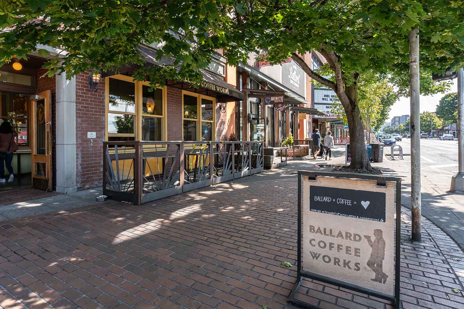 Sidewalk view of Ballard Coffee Works and neighboring shops on a leafy street in Ballard, Seattle.