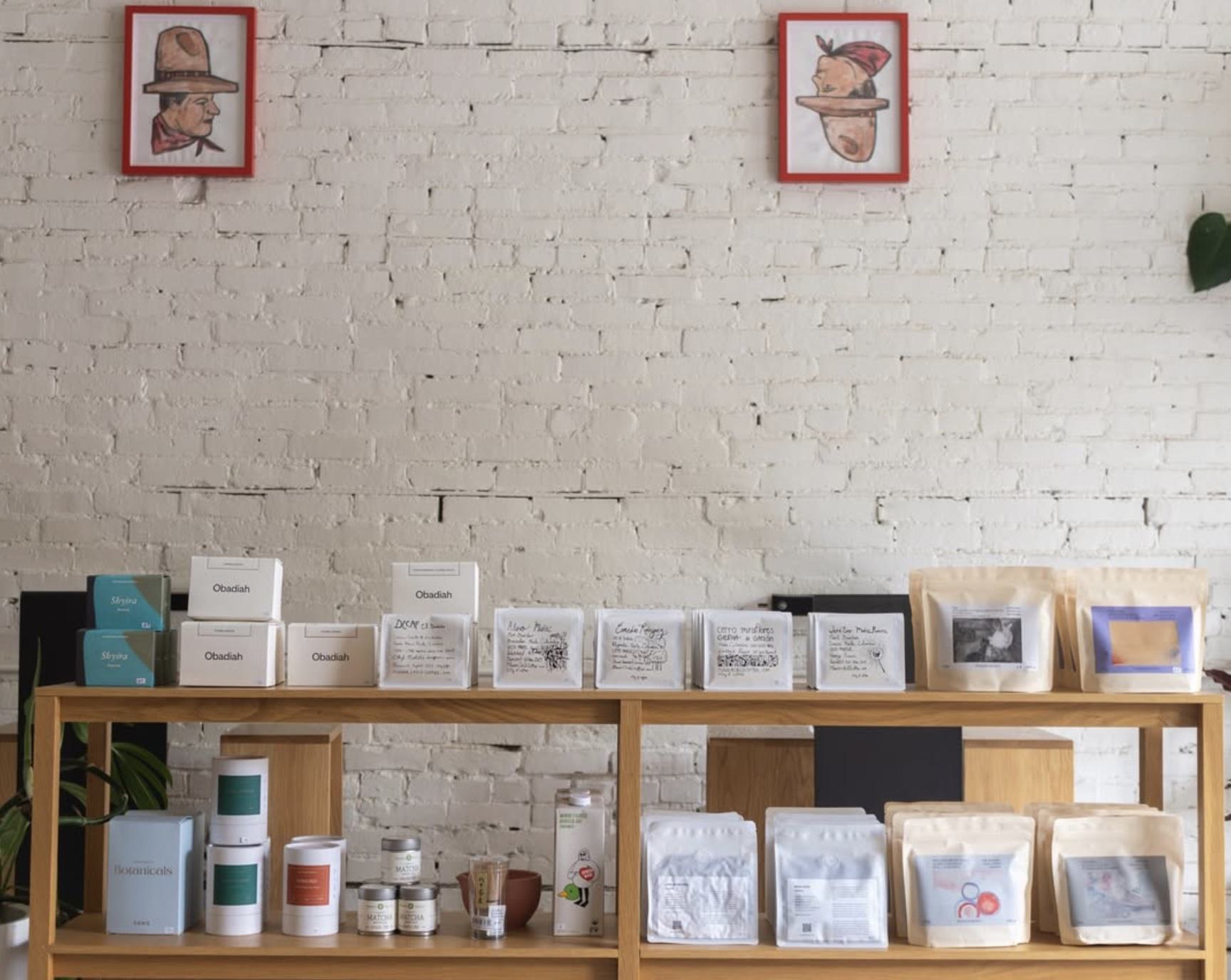 interior of homage coffee with white painted brick walls and a curated display of artisan roasted coffee and other wares for sale