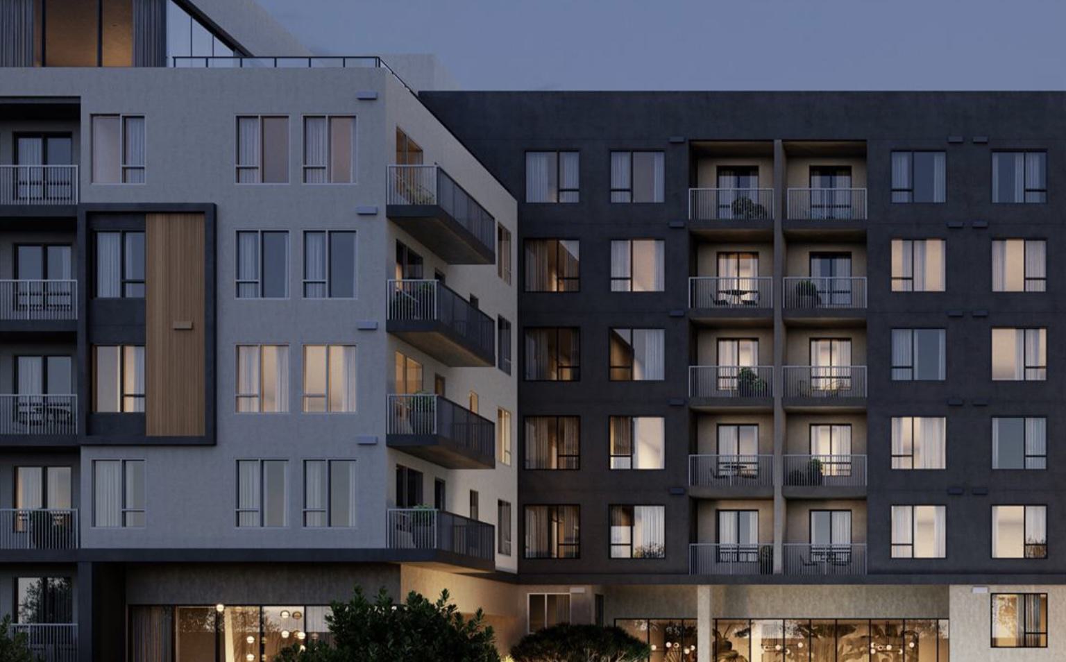 Evening view of Rowyn’s exterior showing a modern facade with a mix of light and dark tones, private balconies with minimalist railings, and warm light glowing through the floor-to-ceiling windows of multiple residences.
