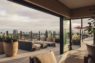 Rooftop terrace at Denizen in Hillcrest with glass-panel railings, cushioned lounge seating around a modern fire pit, and views of the city and coastline in the distance.