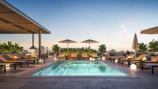 Rooftop pool deck at Denizen in Hillcrest at dusk, featuring a glowing turquoise pool, modern lounge chairs, umbrellas, and city skyline views in the background.