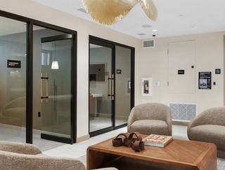 Glass-walled meeting rooms open off the coworking lounge at Denizen, featuring modern wood and black trim doors