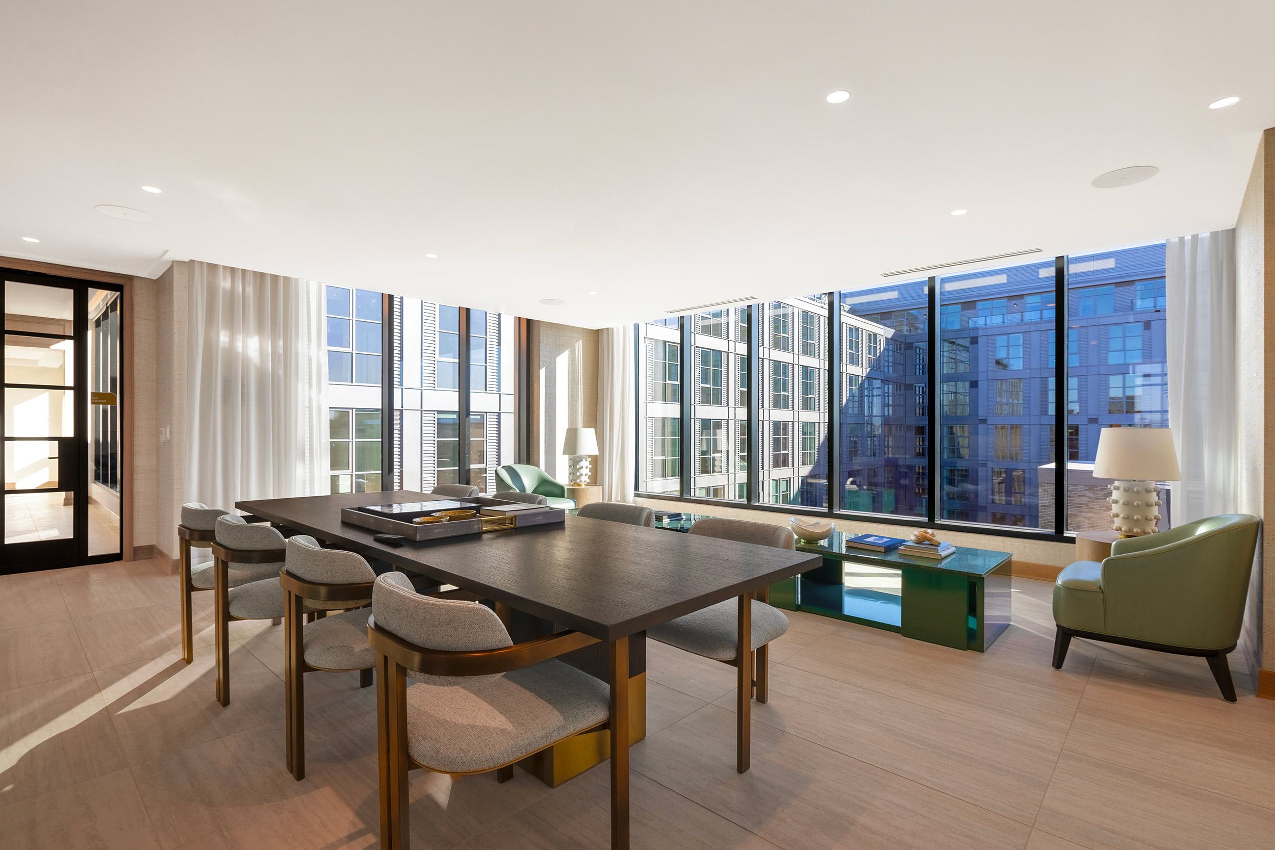 Light-filled private dining and meeting space with a dark wood table, gray chairs, floor-to-ceiling windows, and sweeping views of the surrounding cityscape.