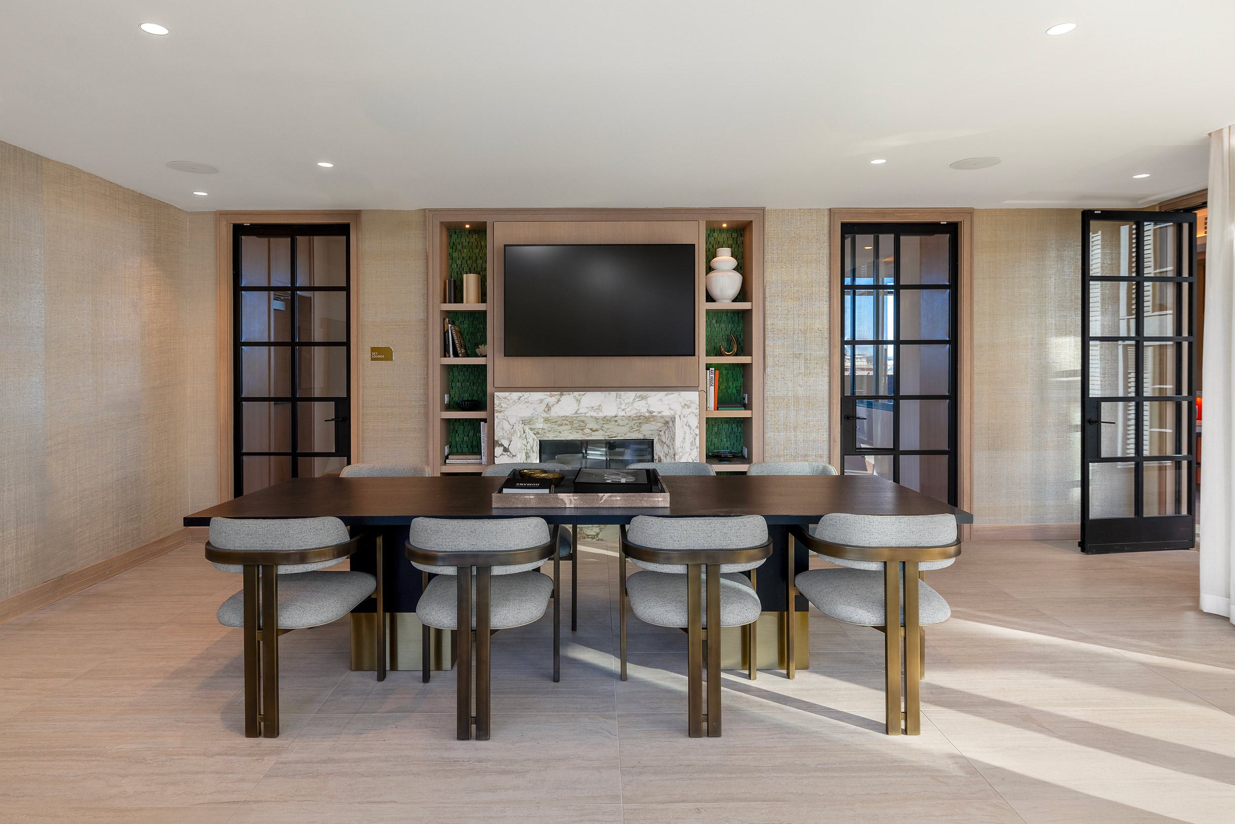 Private dining and meeting room with a dark wood table, gray upholstered chairs with brass accents, marble fireplace, built-in shelving, and glass-paneled doors.