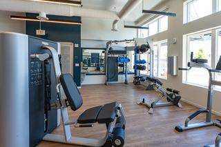 Spacious Admiral’s Cove fitness center featuring Technogym strength equipment, free weights, and large windows that fill the room with sunlight.