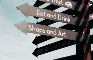 Directional street signs in RiNo Denver pointing to “Eat and Drink,” “Shops and Art,” and “38th & Blake Station.