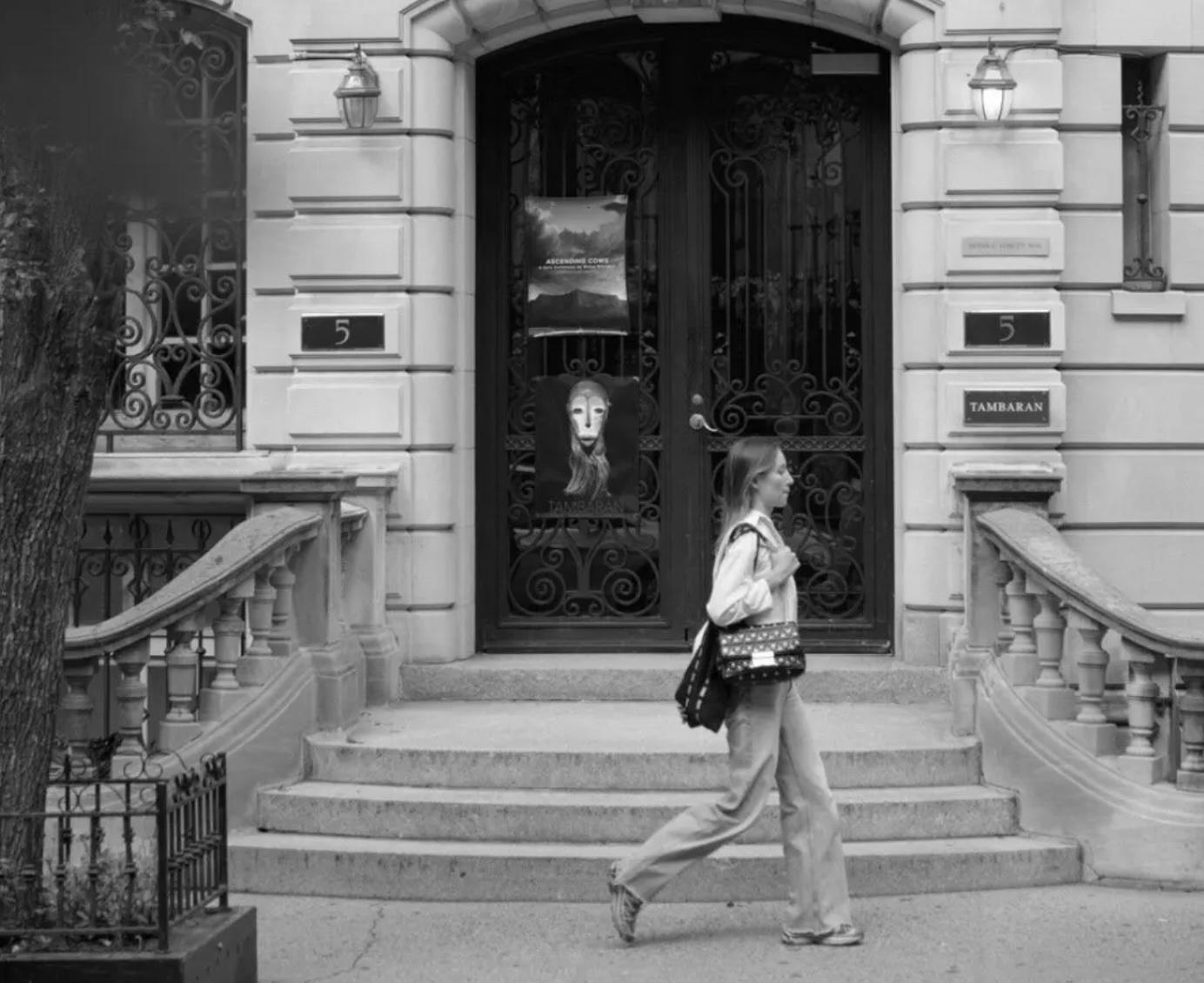black and white photo of a woman walking in front of an elegant ues brownstone art gallery