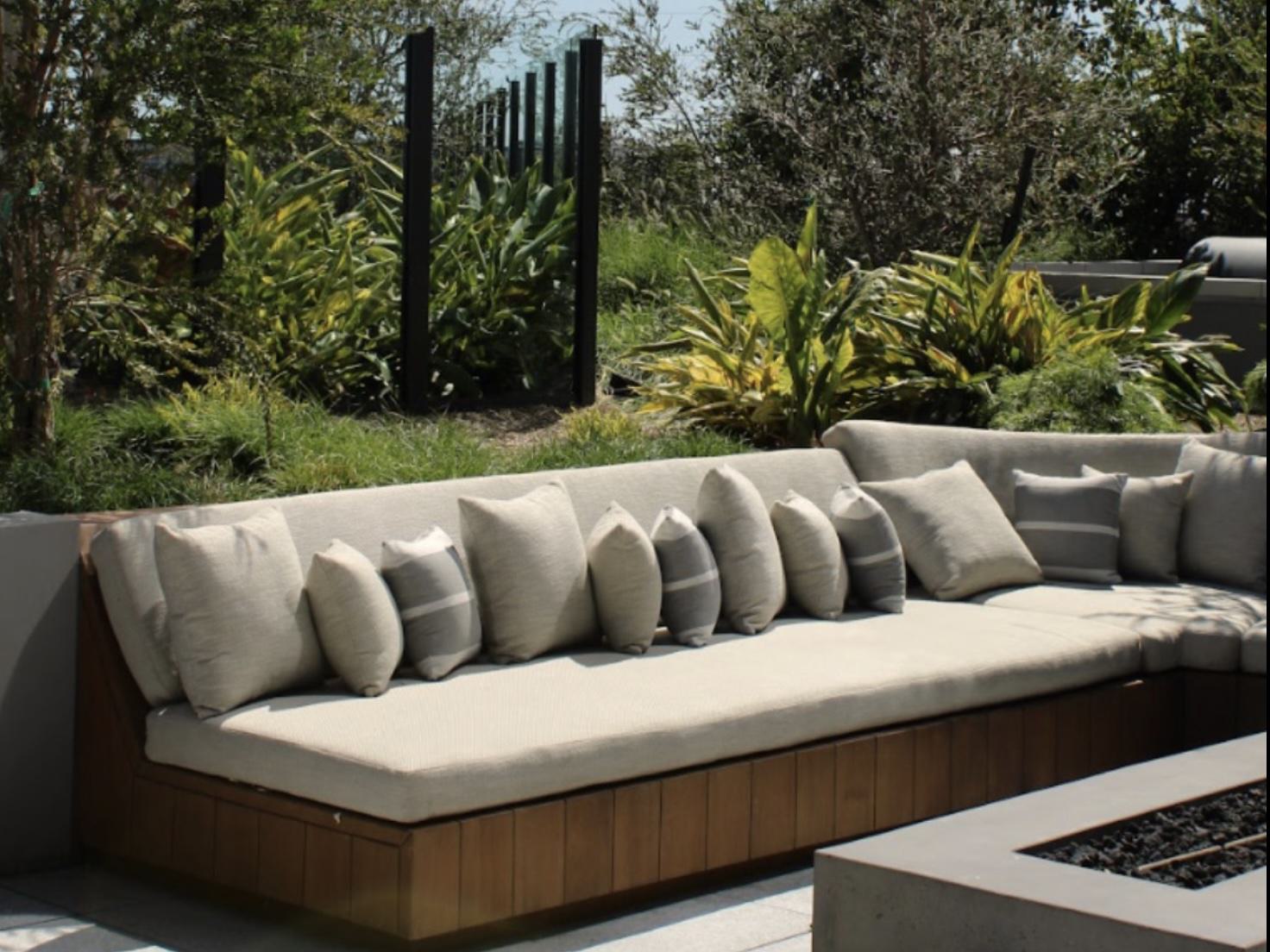 Modern terrace with outdoor kitchen, dining tables, and striking copper circular light fixtures suspended above lush plantings and contemporary woven seating.