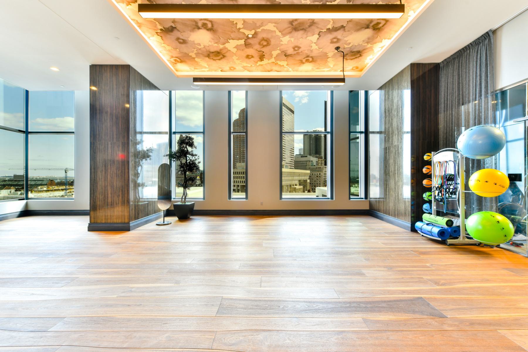 Yoga and Pilates studio with wood floors, floor-to-ceiling windows, a decorative backlit ceiling, and neatly organized stability balls, mats, and training gear.