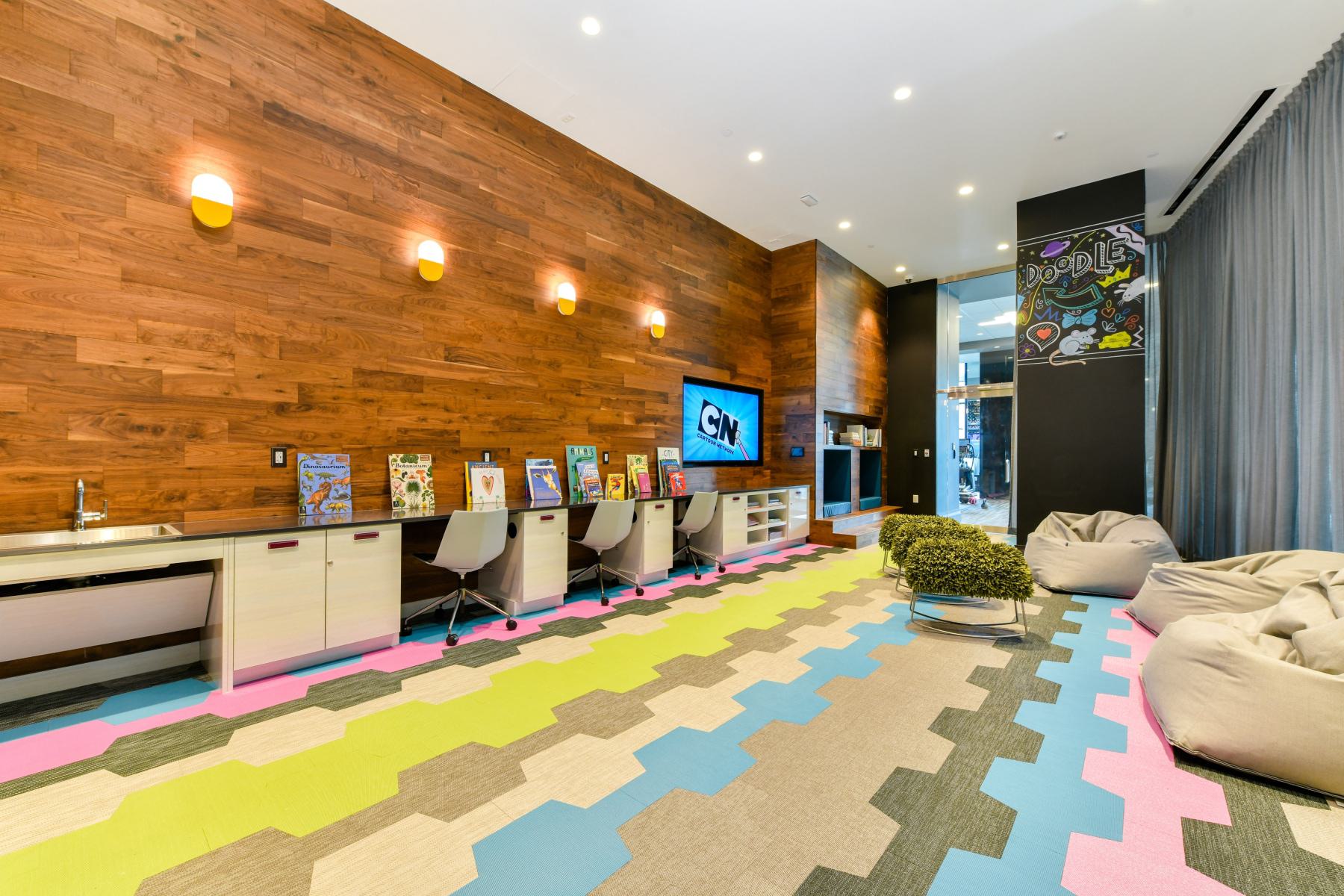 Children’s play space with bean bags, grass-textured stools, chalkboard wall with playful lettering, and shelves filled with books and toys.