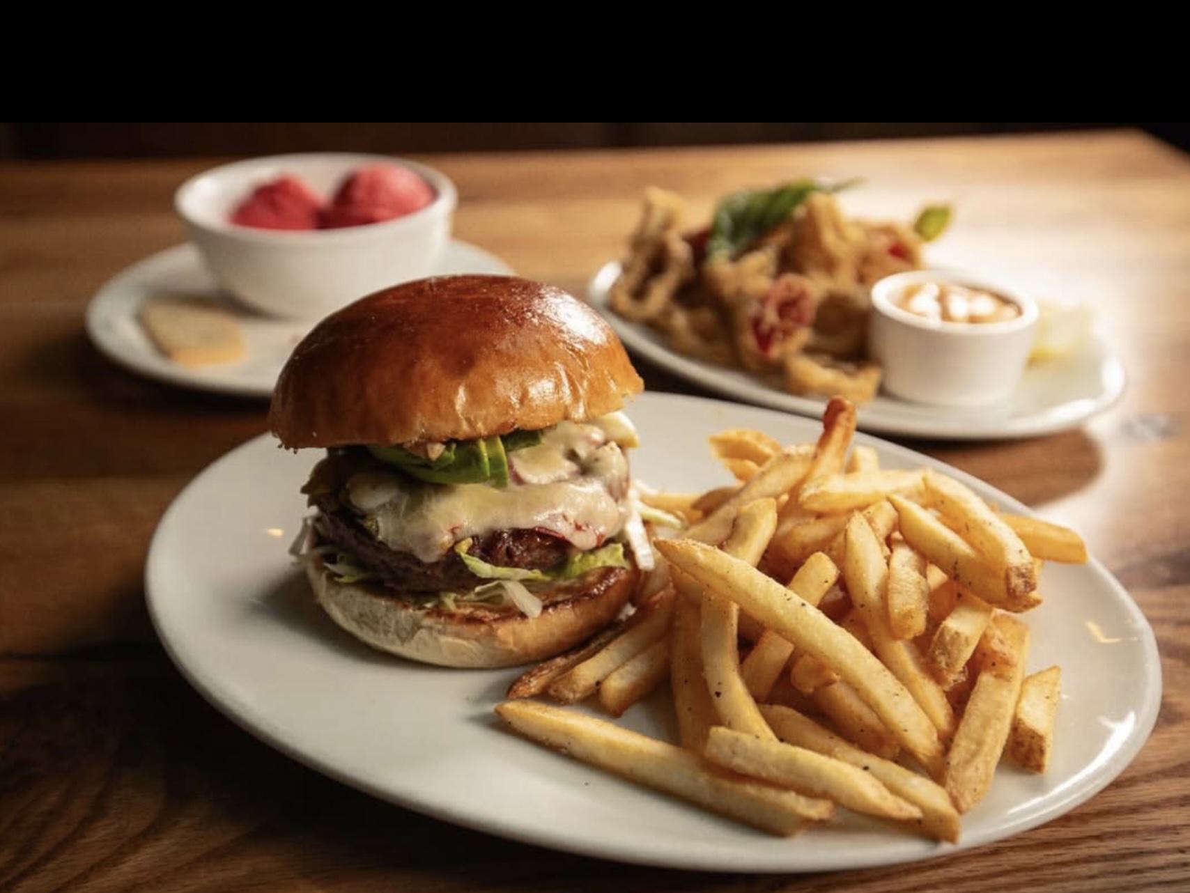 Close-up of a cheeseburger with jalapeños, melted cheese, lettuce, and a glossy brioche bun, served with golden fries on a white plate at The Victor in South Lake Union.