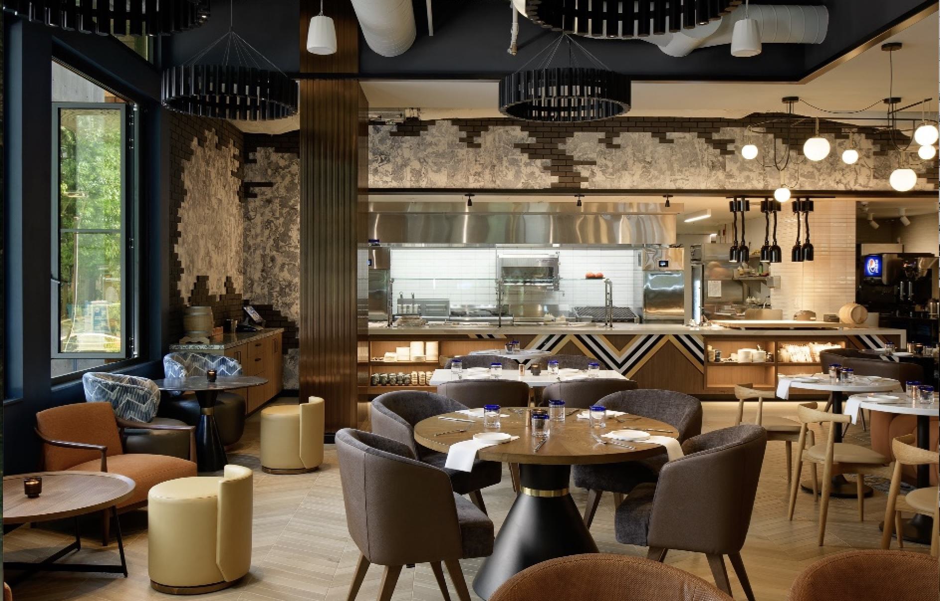 Chic interior of Otium in South Lake Union, featuring round wooden tables, cushioned chairs, modern pendant lighting, and an open kitchen with geometric tile accents.