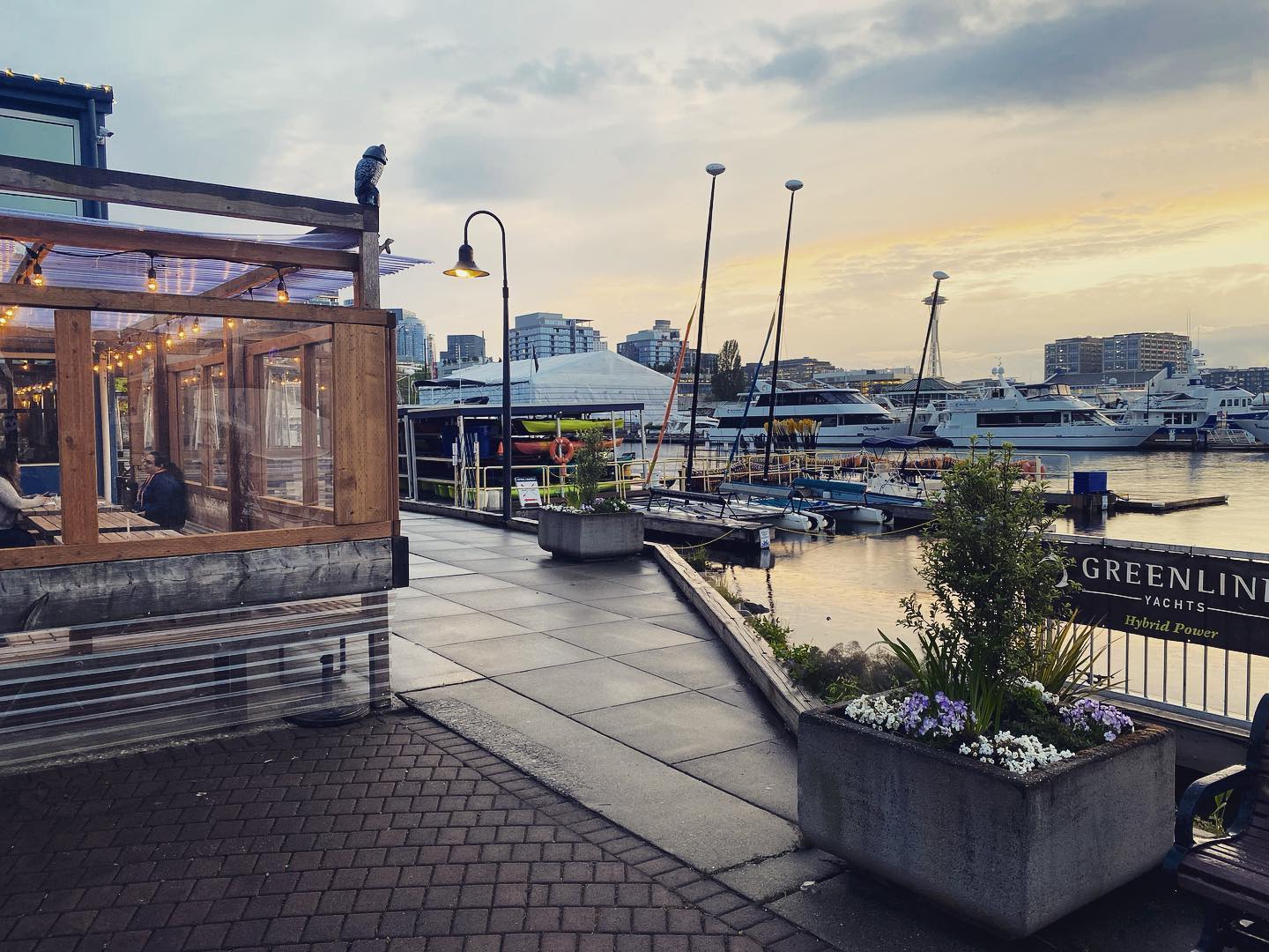Waterfront dining patio at White Swan Public House at sunset with weathered wood restaurant structure, string lights, yacht marina, and Seattle city skyline visible across Lake Union waters.